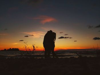 Silhouette man standing on beach against sky during sunset