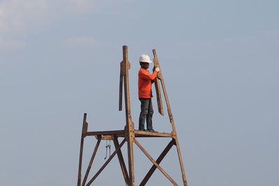 Low angle view of man standing on ladder against sky