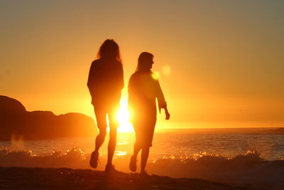 Silhouette friends on beach against sky during sunset