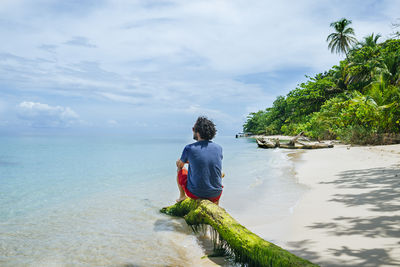 Panama, bocas del toro, cayo zapatilla, man sitting on tree trunk on the beach