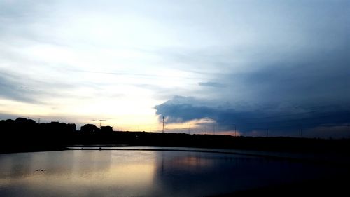 Reflection of silhouette trees in calm lake at sunset