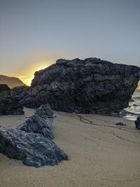 Rock formation on beach against sky during sunset