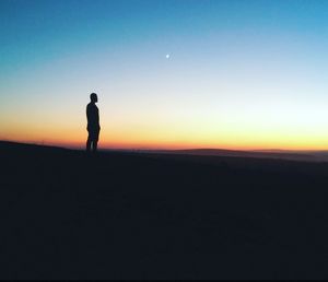 Silhouette man standing on field against clear sky during sunset