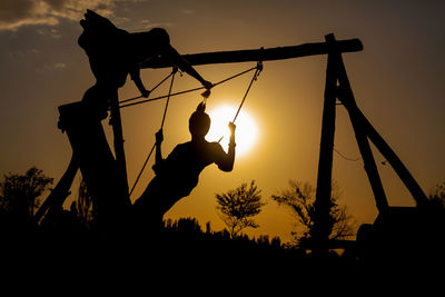 Silhouette of children on swing at sunset