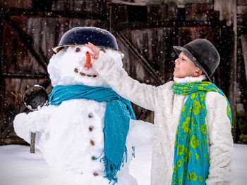 Rear view of kid and snowman during winter