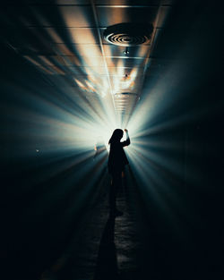 Rear view of silhouette person walking in illuminated tunnel