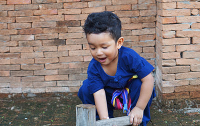 Baby boy holding tool while crouching against brick wall