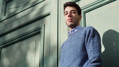 Portrait of handsome young man standing against closed wooden door