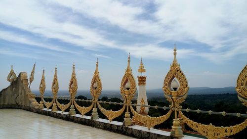 Patterned golden railing with lighting equipment against sky