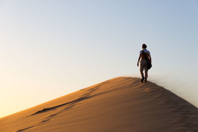 Rear view of mature woman walking on sand dune against clear sky