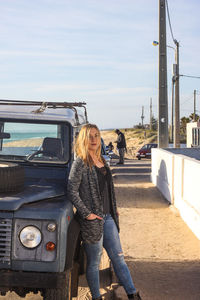 Portrait of woman standing by off-road vehicle against sky