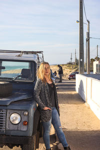 Full length of woman standing by car against sky