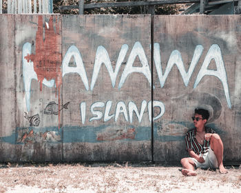 Full length of young man sitting against wall