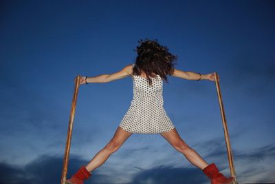 Rear view of woman jumping against sky