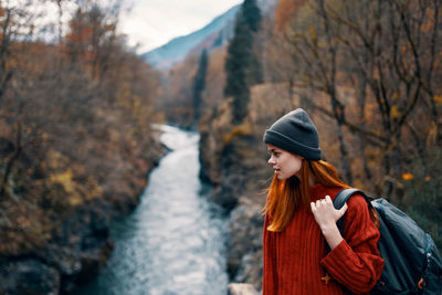 Young woman looking away while standing on tree during autumn