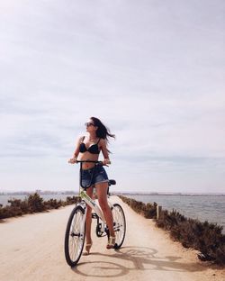 Full length of beautiful woman with bicycle on footpath amidst sea against sky