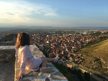 Side view of girl looking at cityscape against sky during sunset