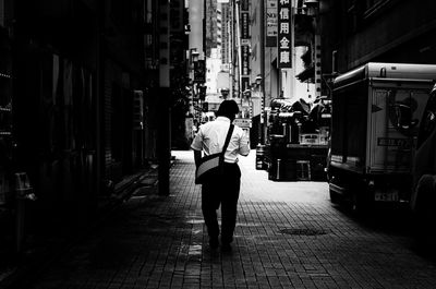 Rear view of man walking on footpath amidst buildings in city