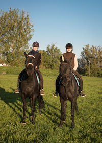 Female jockeys riding horses on grassy field against clear sky