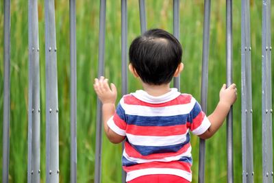 Rear view of boy standing against fence on field