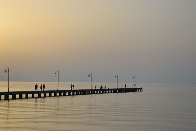 Silhouette people on pier over sea against clear sky during sunset