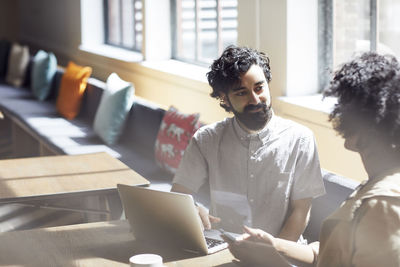 Businessman looking at female colleague while working on laptop computer