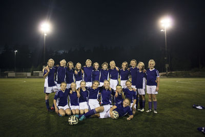 Portrait of girl's soccer team on illuminated field against sky