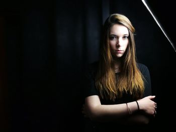 Portrait of young woman standing against black background