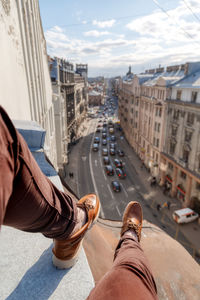 Man legs in burgundy trousers and brown loafers. male sitting on edge of roof in saint petersburg