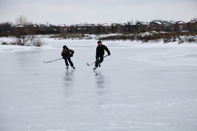 Boys playing ice hockey on rink against sky