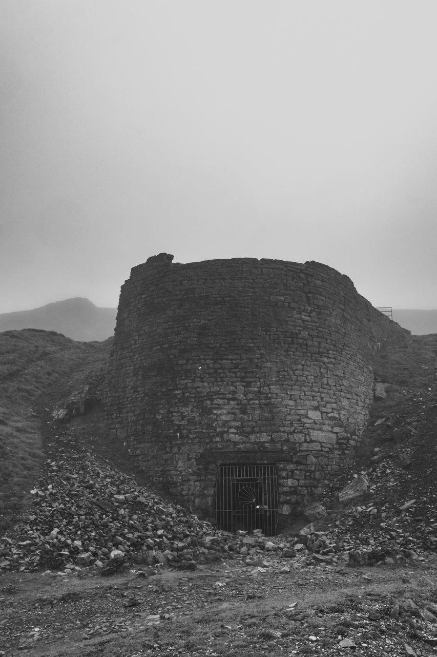 black and white, sky, rock, monochrome, hill, architecture, landscape, nature, land, environment, monochrome photography, no people, history, built structure, scenics - nature, the past, travel destinations, outdoors, travel, building exterior, non-urban scene, beauty in nature, sea, building, tourism, tranquility, fog, horizon, day, black, ruins, cloud, ancient
