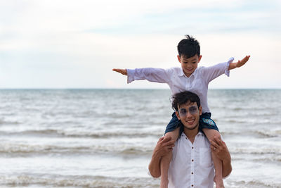 Man carrying boy on shoulder while standing at beach