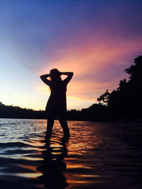 Silhouette woman standing on beach against sky during sunset