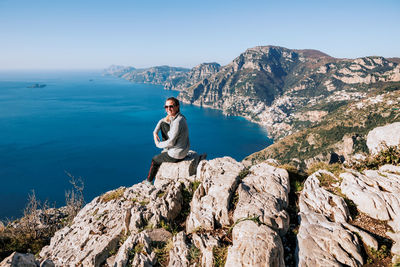 Side view of woman standing on rock against sky