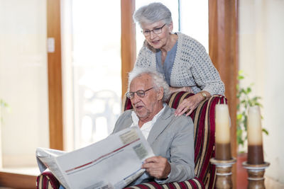 Senior man and woman sitting in library, reading newspaper