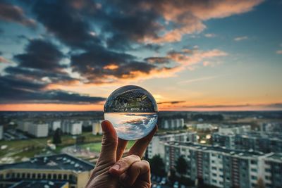 Close-up of hand holding crystal ball against cityscape during sunset