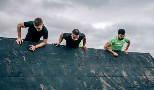 Male friends climbing on wall against sky