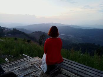 Rear view of woman leaning on table at mountain against sky during sunset