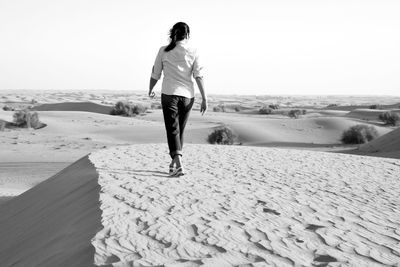 Woman walking on sand at beach against clear sky