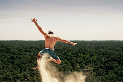 Full length of shirtless man jumping over landscape against sky