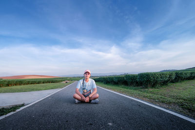 Young woman sitting on road against sky