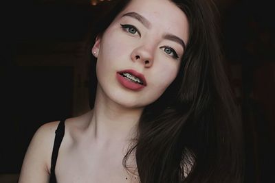 Close-up portrait of young woman with braces in darkroom