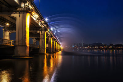 Illuminated bridge over river against sky at night