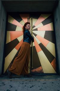 Full length portrait of smiling young woman standing against wall