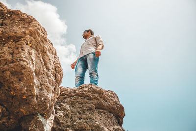 Low angle view of man standing on rock against sky