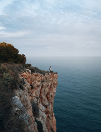 Scenic view of woman standing on cliff against sea and sky