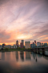 River by buildings against romantic sky at sunset