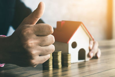 Cropped hands of man with model house and coins showing thumbs up sign