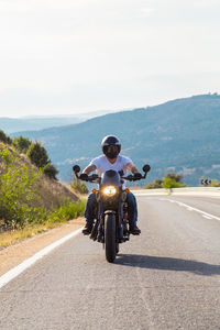 Young man riding motorcycle on road against sky