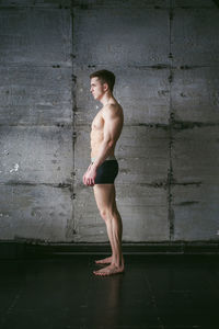 Side view of shirtless muscular man standing by wall